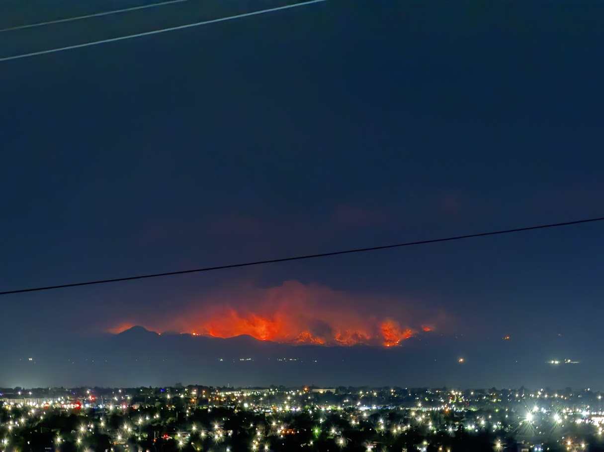 A nighttime view of Utah mountains across the valley, lit up orange with bright flames on the mountains.
